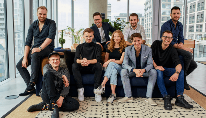 A group photo of the entire nine-person team on a couch in a chillout room.