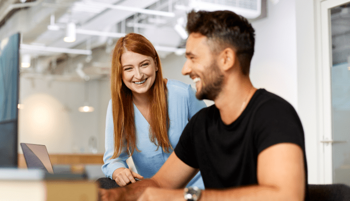 A man and a woman laughing at a simple bug in the code that no one could find.